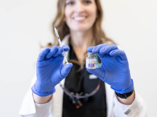 Woman with gloved hands holding needle and bottle