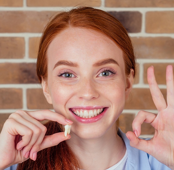 Smiling woman holding up extracted wisdom tooth