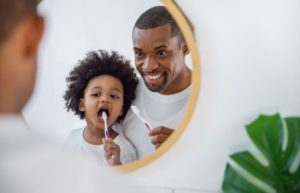 young boy brushing teeth with dad 